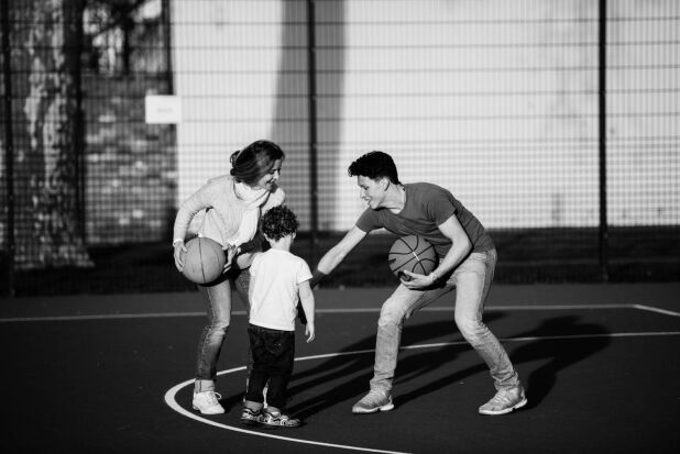 a woman and two children playing basketball on a court
