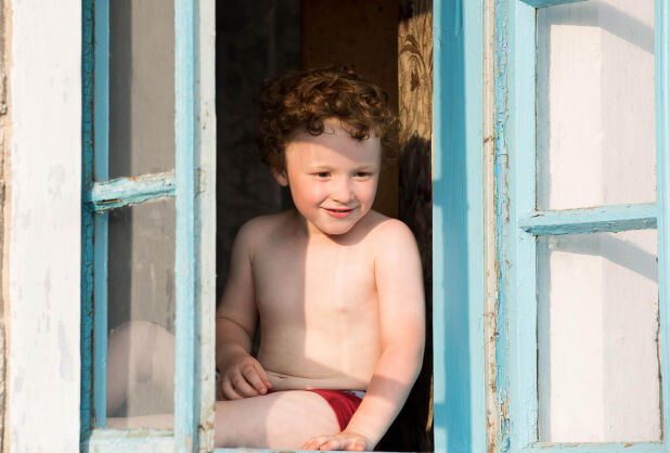 a young boy sitting in a window looking out